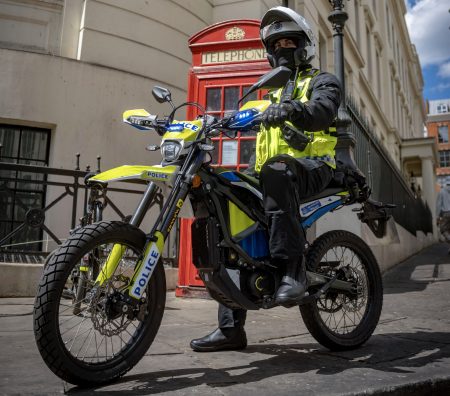 Ein Metropolitan-Police-Beamter in gelber Warnweste sitzt auf seinem gelb-schwarzen Sur-Ron-Ultra-Bee-Polizeimotorrad mit Aufschrift Police vor einer roten Londoner Telefonzelle