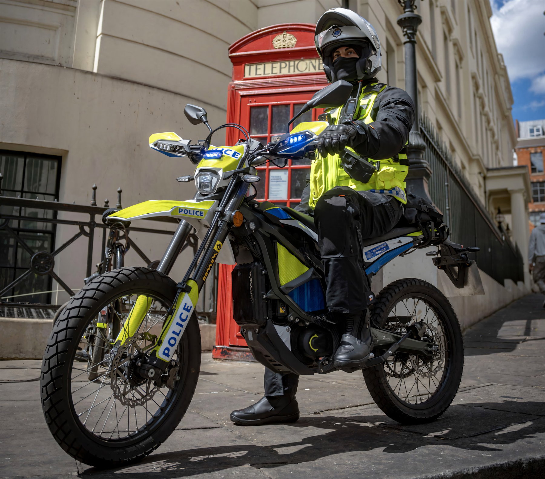 London Police Ride the Sur-Ron Ultra Bee: 25 Bikes Against Phone Snatching 1 Ein Metropolitan-Police-Beamter in gelber Warnweste sitzt auf seinem gelb-schwarzen Sur-Ron-Ultra-Bee-Polizeimotorrad mit Aufschrift Police vor einer roten Londoner Telefonzelle