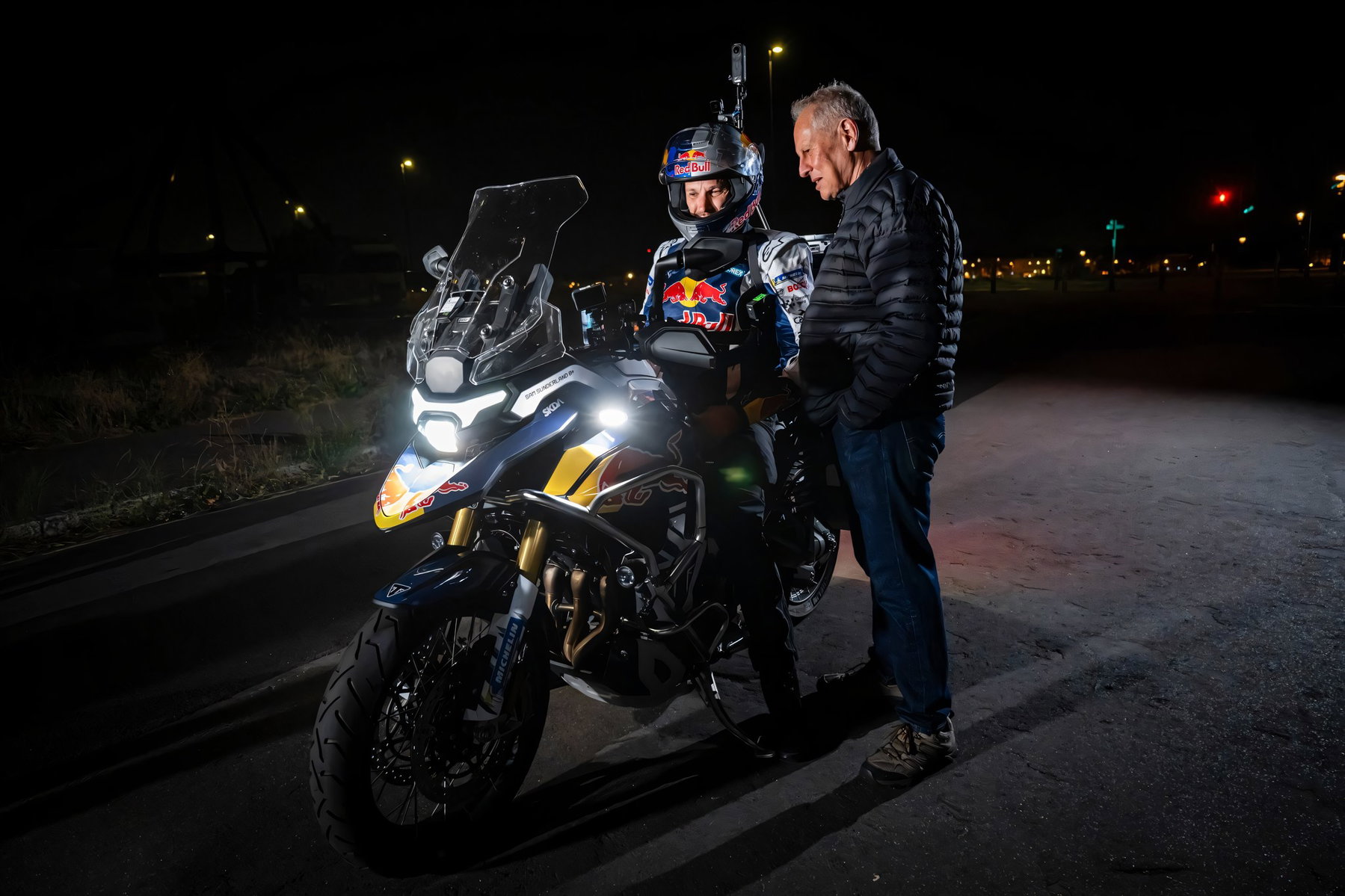 Sunderland verrät Triumphs Geheimnis: Neue Tiger 1200 auf Weltrekordfahrt 1 Nahaufnahme bei Nacht: Sam Sunderland auf der Triumph Tiger 1200 mit beleuchtetem LED-Scheinwerfer im Gespraech mit Kevin Sanders