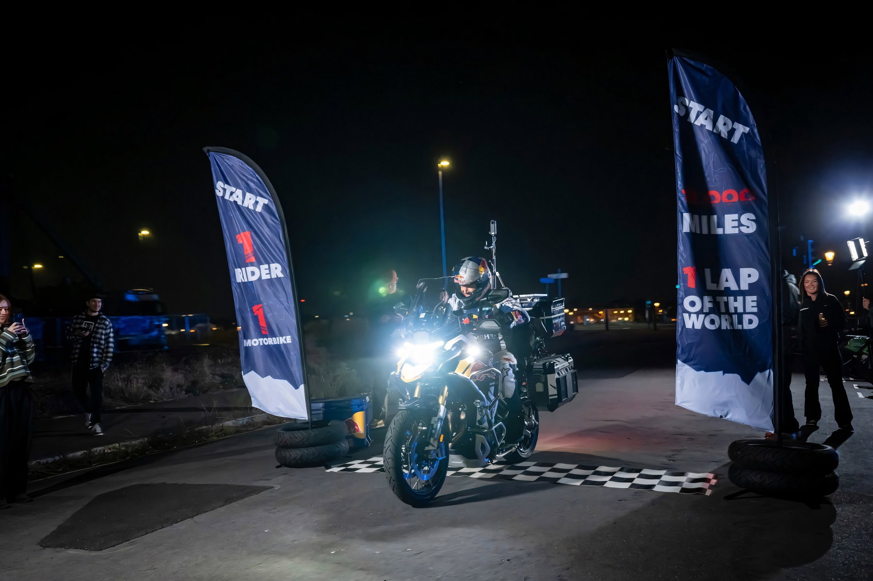 Sunderland verrät Triumphs Geheimnis: Neue Tiger 1200 auf Weltrekordfahrt 6 Sam Sunderland faehrt bei Nacht auf der Triumph Tiger 1200 ueber die Startlinie in Greenwich, Startbanner mit Aufschrift 1 Rider 1 Motorbike und 18.000 Miles