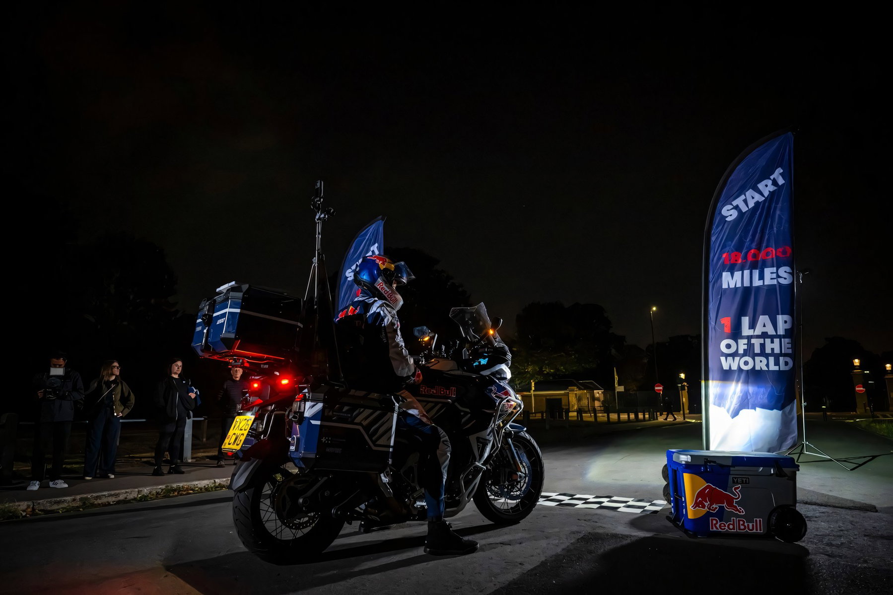 Sunderland verrät Triumphs Geheimnis: Neue Tiger 1200 auf Weltrekordfahrt 5 Weite Nachtaufnahme von Sam Sunderland auf der Triumph Tiger 1200 an der Startlinie in Greenwich mit Zuschauern und Red-Bull-Kuehlbox