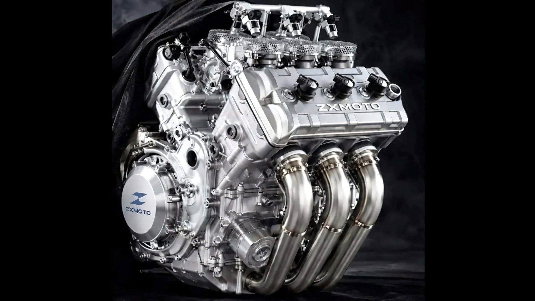 ZXMoto V5-Superbike für 2028: Was bestätigt ist und was nicht 1 ZXMoto V5-Motor 2028 - das kursierende Foto des neuen V5-Kompressormotors mit drei nach vorn und zwei nach hinten geneigten Zylindern, freigestellt vor dunklem Stoffhintergrund, ZXMOTO-Schriftzug auf dem Zylinderkopfdeckel