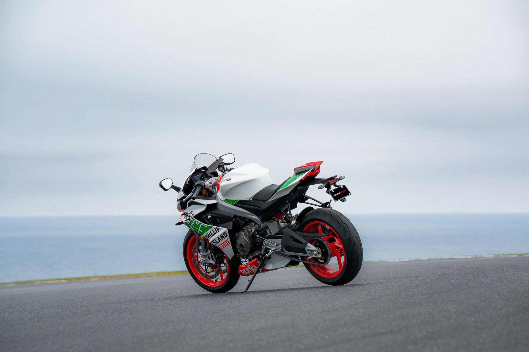 RS 660 Phillip Island Tribute: Aprilias Sondermodell zum MotoGP-Abschied 3 Aprilia RS 660 Phillip Island Tribute schräg von hinten links mit roten Felgen und grün-weißem Heck an der Küste von Phillip Island