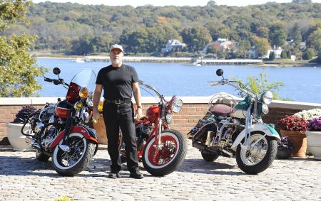 Billy Joel steht zwischen drei klassischen Motorrädern auf einer Terrasse am Wasser – Archivfoto