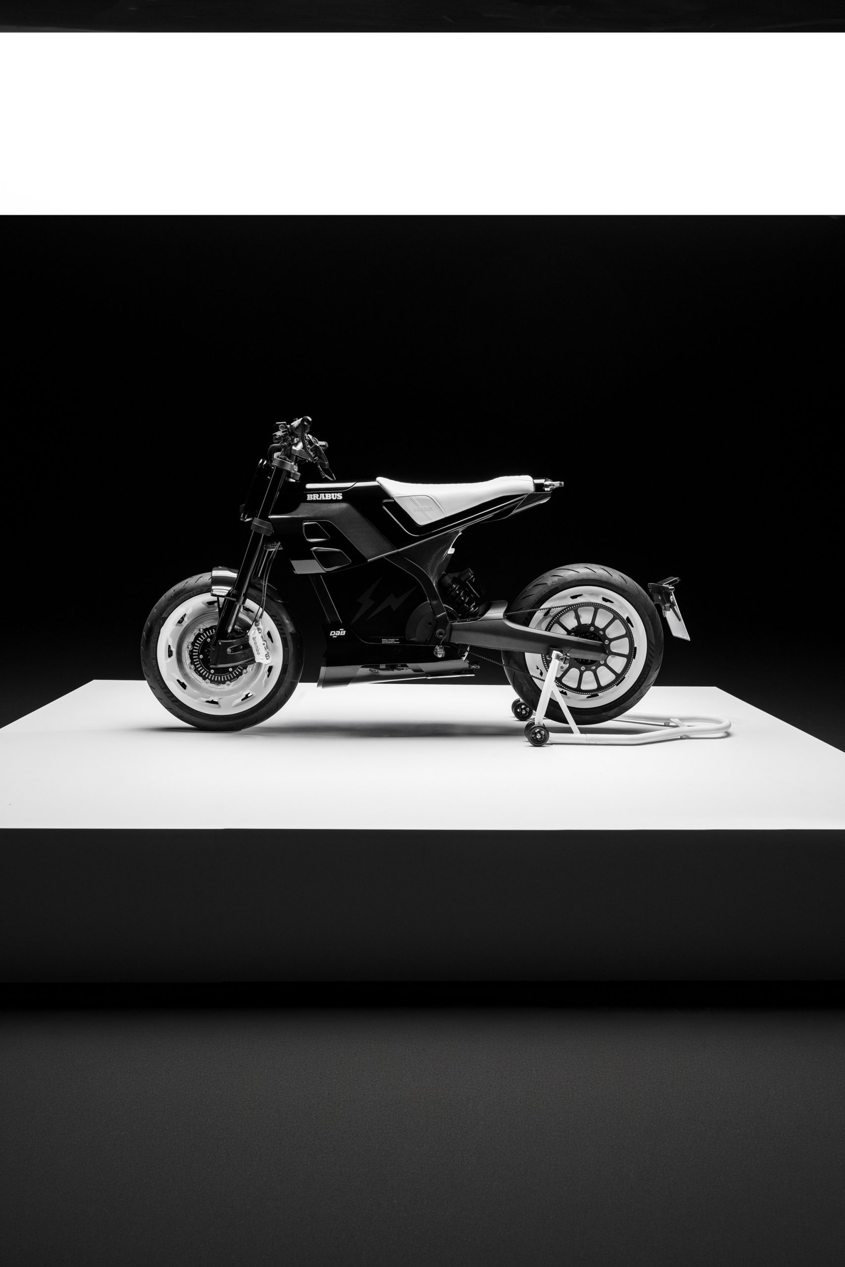 BRABUS URBAN E FRAGMENT EDITION: Almost 15,000 Euros More for Fujiwara's Design 2 BRABUS Urban-E Fragment Edition 2026 – Seitenansicht von links mit Monocoque-Tank-Sitzverkleidung, Carbon-Seitenteilen und Montageständer auf weißem Podest