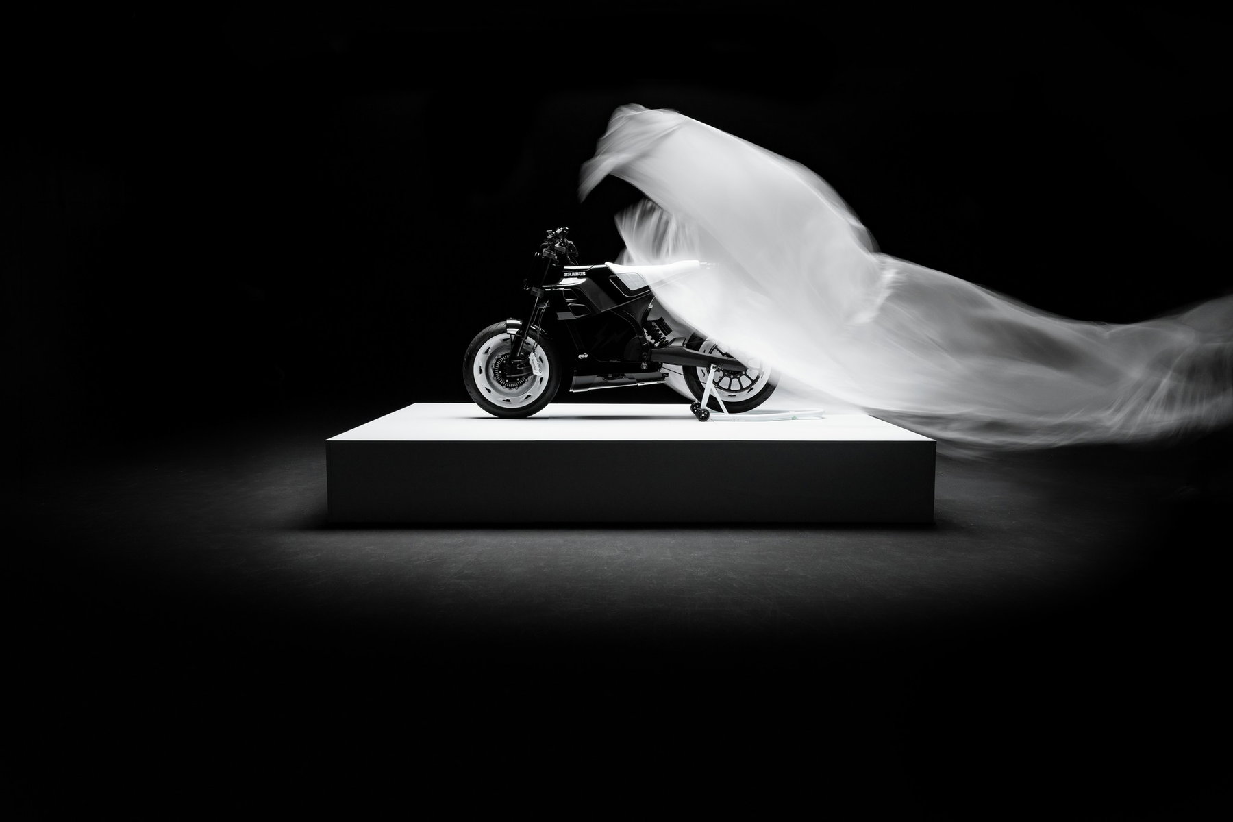 BRABUS URBAN E FRAGMENT EDITION: Almost 15,000 Euros More for Fujiwara's Design 3 BRABUS Urban-E Fragment Edition 2026 – Enthüllung auf dem Podest – die weiße Plane wird vom Motorrad gezogen