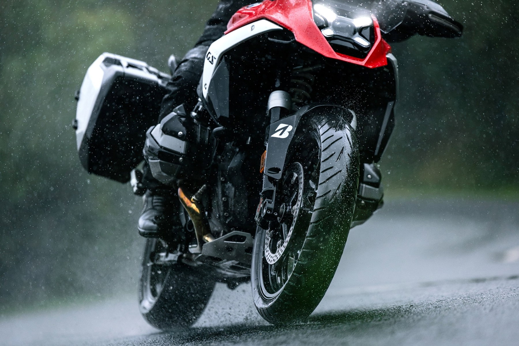 Bridgestone Battlax Adventure A42 – BMW-Reiseenduro mit Seitenkoffern in Schräglage auf regennasser Straße, Gischt spritzt vom Vorderreifen