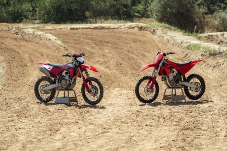 Ducati Desmo450 MX und Desmo450 MX Factory 2027 – Factory-Version mit Ducati-Corse-Lackierung (links) und Standardmodell in Ducati Red (rechts) auf Montageständern an der Motocross-Strecke