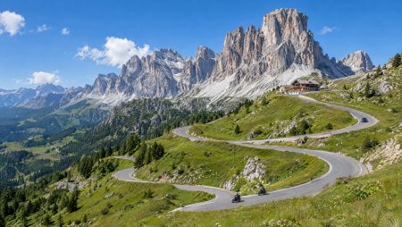 Zwei Motorräder in den Serpentinen einer Dolomiten-Passstraße unter hellen Kalkfelsen, Berghütte an der Passhöhe, blauer Sommerhimmel