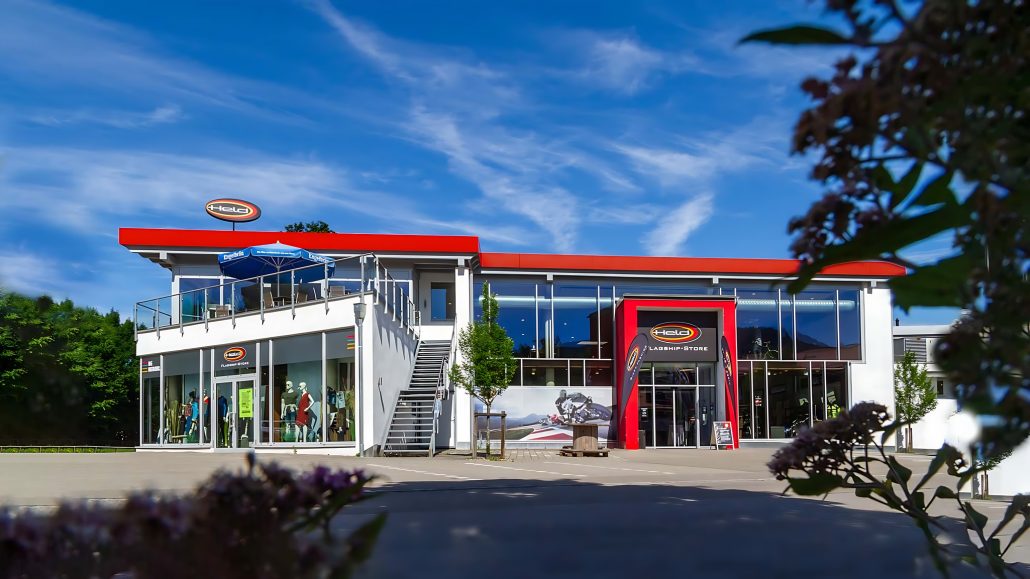 Held übernimmt Hans van Wijk Motoren: Warum der Hersteller Läden kauft 5 Held Flagship-Store in Sonthofen – Ladengebäude mit großer Glasfront und Dachterrasse bei blauem Himmel