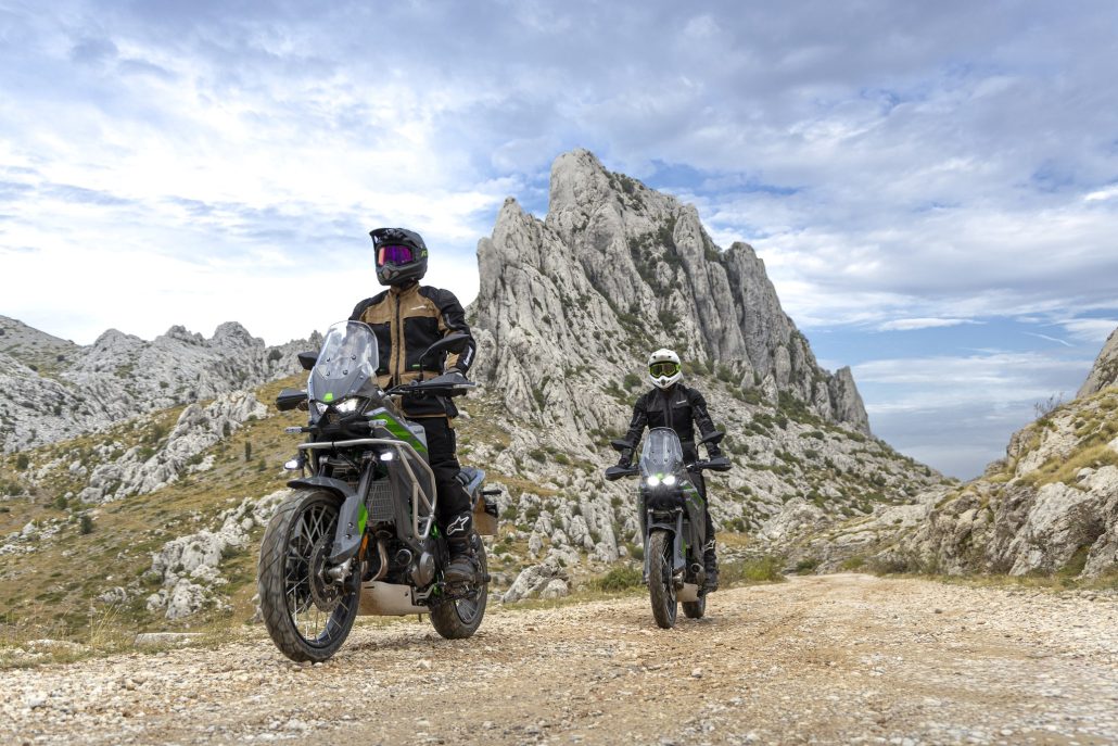 Zwei Kawasaki KLE650 SE 2027 in Pearl Storm Gray auf einer Schotterpiste vor einem schroffen Felsgipfel