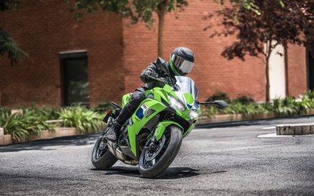 Kawasaki Ninja 650 2027 in Lime Green in Schräglage in einer Kurve vor einer roten Backsteinwand, Fahrer mit grün-schwarzem Helm