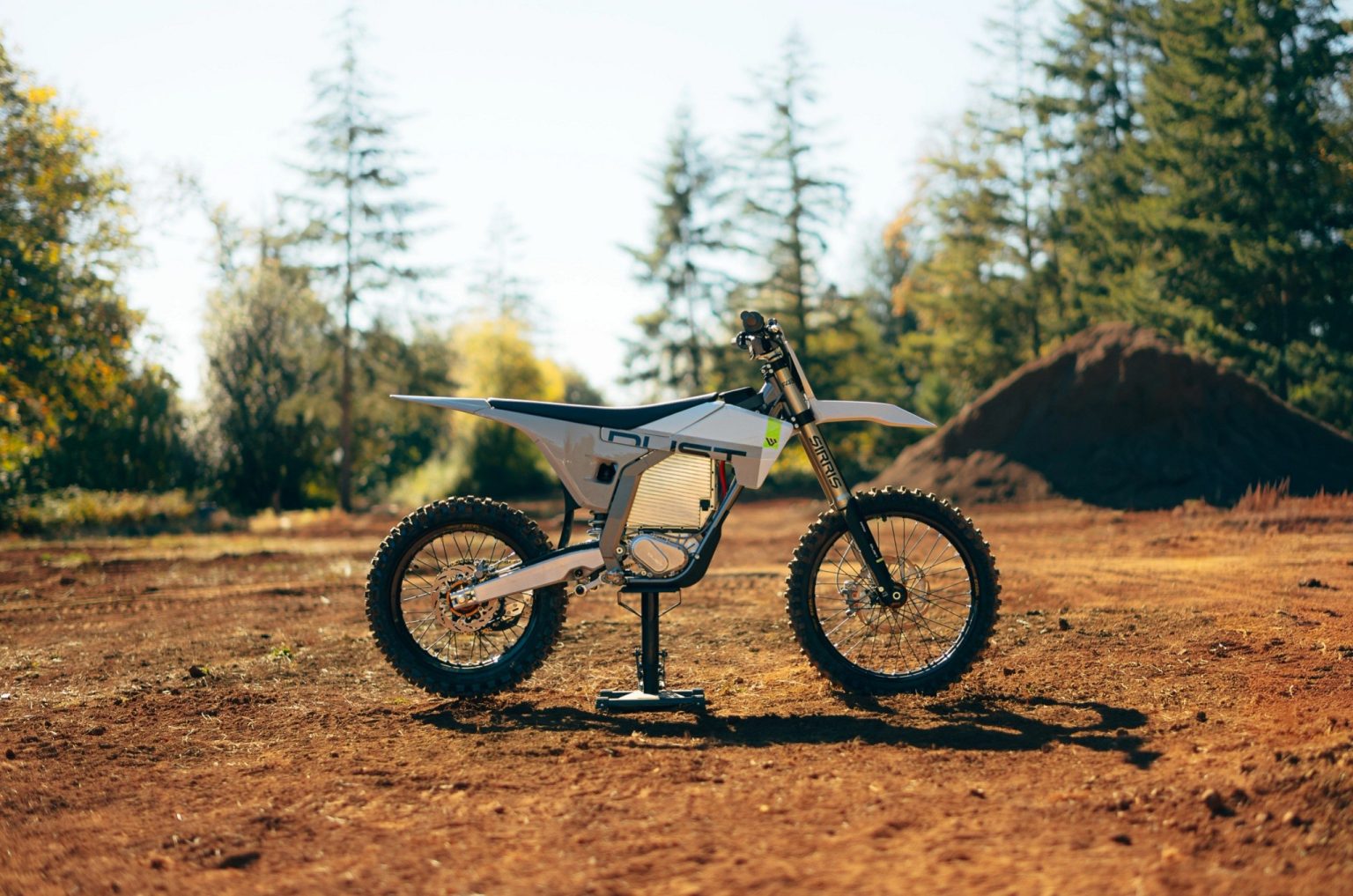 LiveWire Dust Hightail Elektro-Enduro in Weiß auf Ständer in einer Offroad-Strecke vor Nadelbäumen