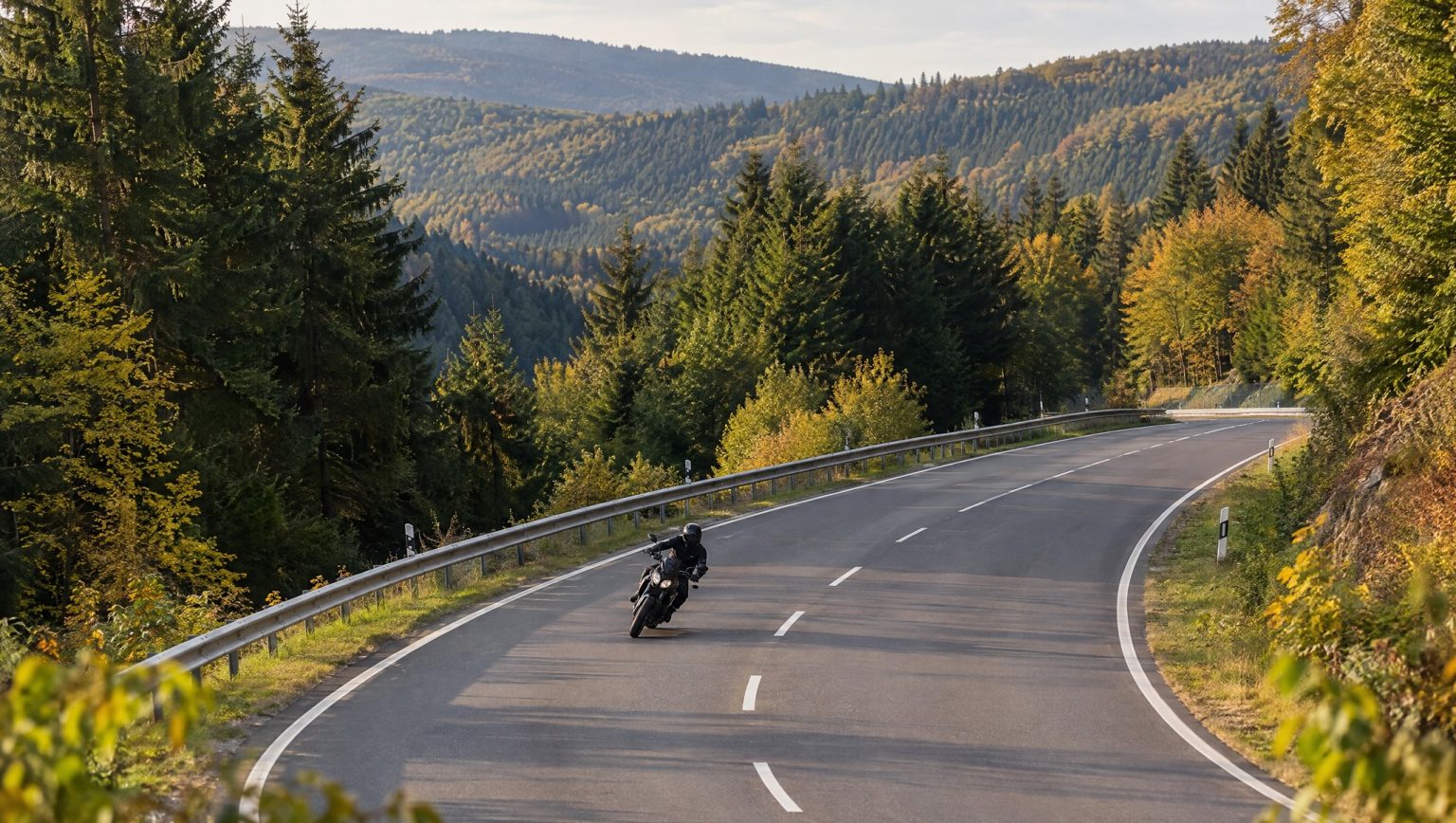 Lützel on the B62: What Is Behind the Rise in Motorcycle Accidents Motorradfahrer in Schräglage auf breiter, kurviger Bundesstraße mit Leitplanke durch herbstlich bewaldetes Mittelgebirge – Symbolbild zur Lützel (B62) im Siegerland