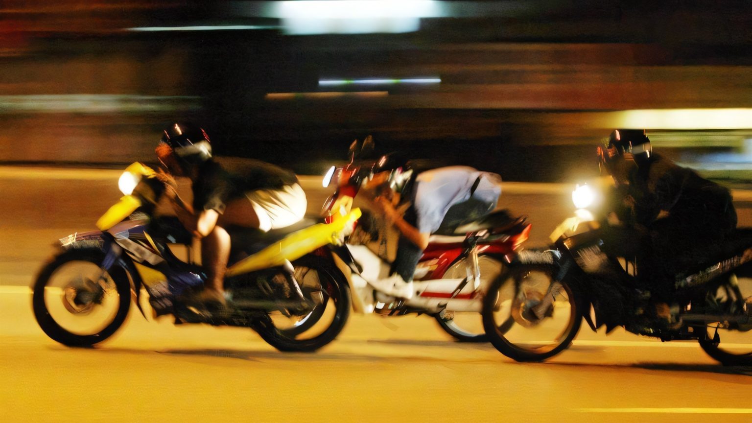Mat Rempit in Penang: 30 Motorräder kassiert, ab November droht Haft Drei Mat Rempit auf Underbone-Motorrädern liefern sich nachts ein illegales Straßenrennen, flach über den Tank geduckt, Hintergrund mit Bewegungsunschärfe