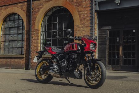 Suzuki GSX-8TT 2027 in Candy Daring Red mit goldenen Felgen und rot-goldenem Tank-Dekor, schräg von vorne vor einer Backsteinfassade