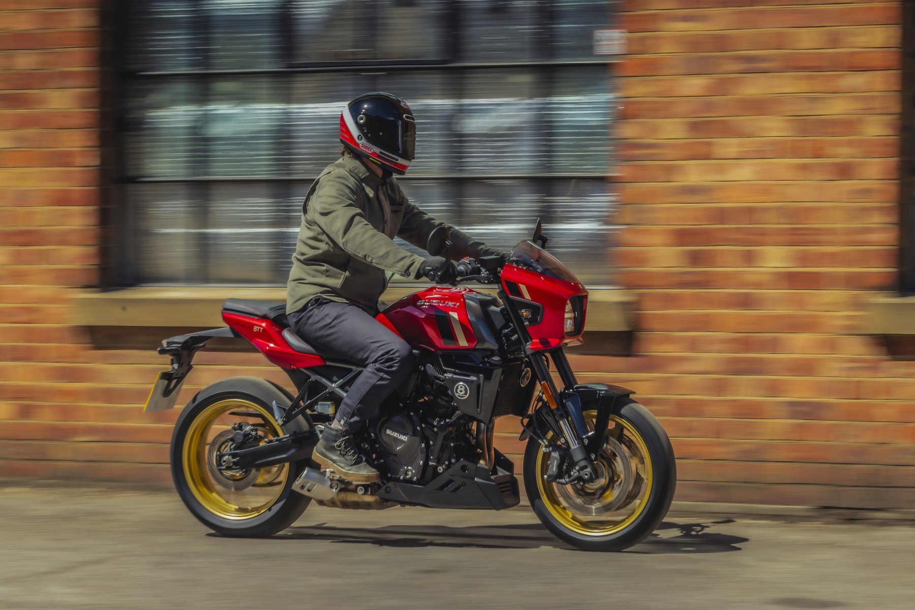 Suzuki GSX-8TT 2027: Rot-Gold-Look und Tempomat, die Technik bleibt 7 Suzuki GSX-8TT 2027 in Candy Daring Red in Fahrt vor einer Backsteinfassade, Mitzieher