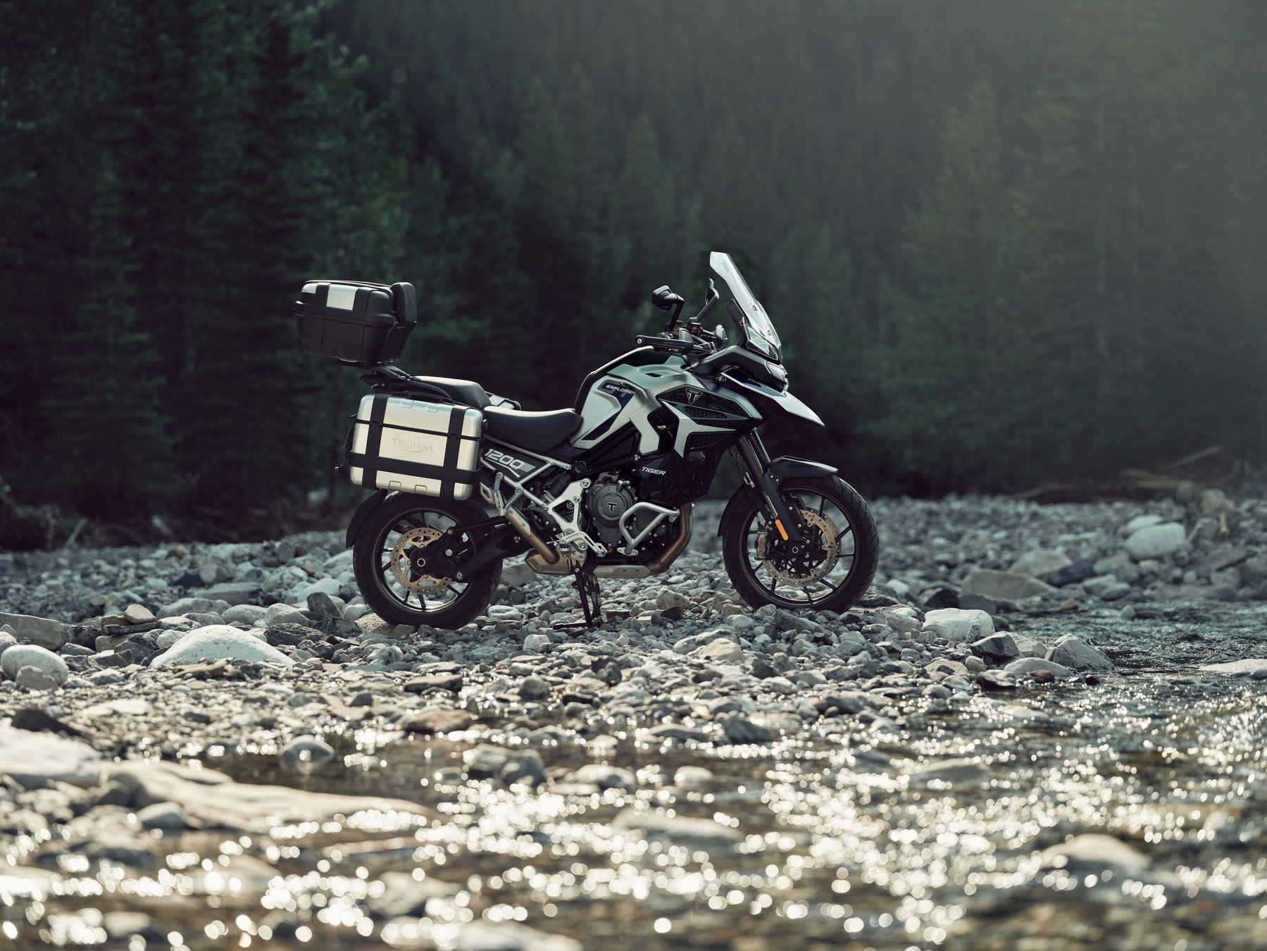 New Triumph Tiger 1200: Why the Rally Now Also Runs a 19-Inch Front Wheel 4 Triumph Tiger 1200 GT Explorer 2027 – in Aluminiumsilber/Pazifikblau mit Topcase und Seitenkoffern im Flussbett