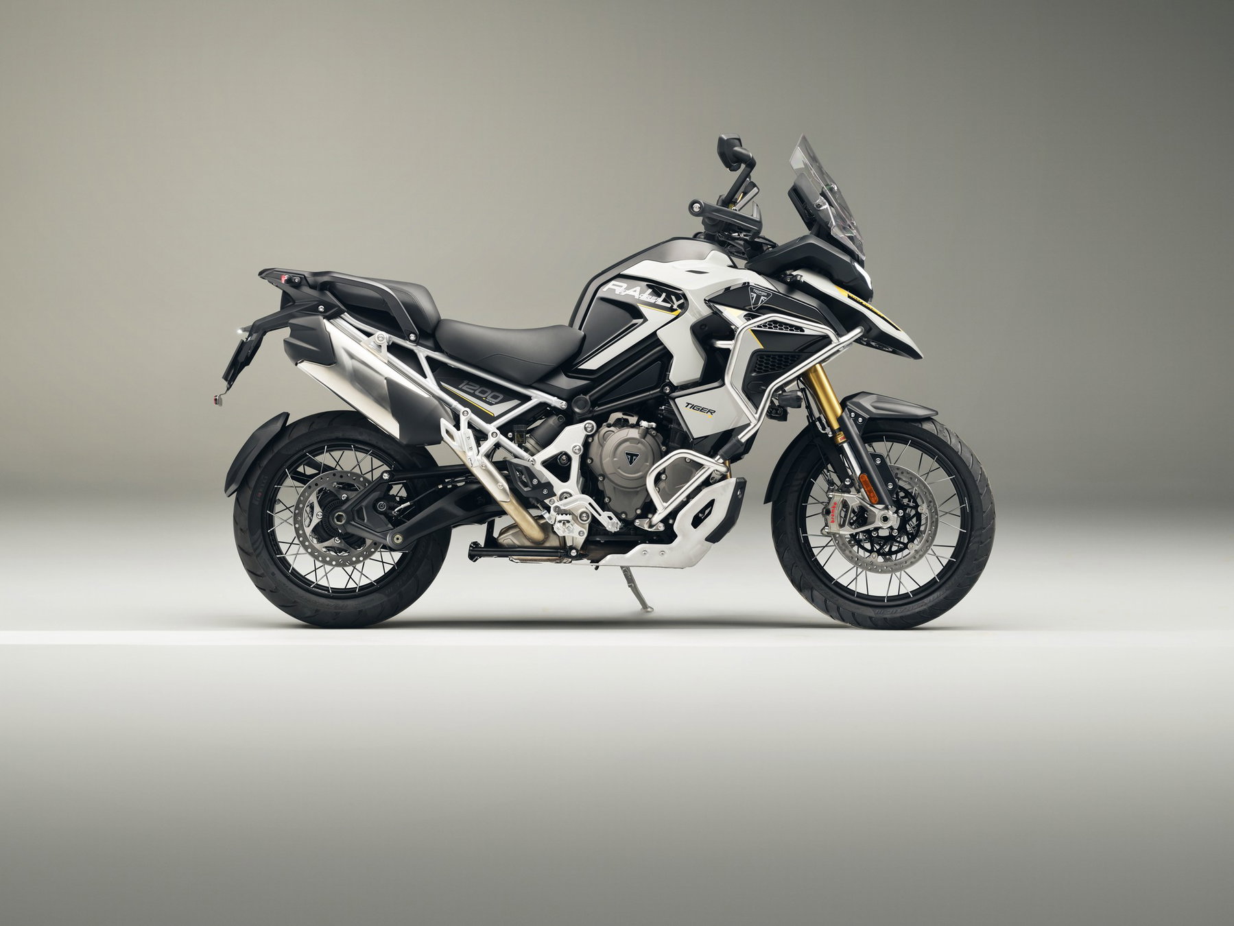 Triumph Neuheiten 2027: Was nach der Bonneville T40 noch kommt 1 Neue Triumph Tiger 1200 Rally Explorer 2027 in Weiß-Schwarz mit Rally-Dekor und goldener Gabel in der Seitenansicht von rechts im hellen Fotostudio