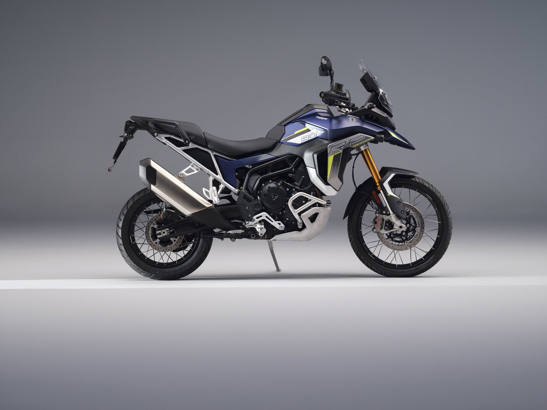 Triumph Neuheiten 2027: Was nach der Bonneville T40 noch kommt 6 Neue Triumph Tiger 900 Rally Pro 2027 in Dunkelblau mit hellgrauem Dekor und gelben Akzenten in der Seitenansicht von rechts im grauen Fotostudio