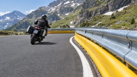 Motorradfahrer fährt auf einem italienischen Alpenpass durch eine Kurve an einer Stahlleitplanke mit durchgehendem gelbem Unterfahrschutz