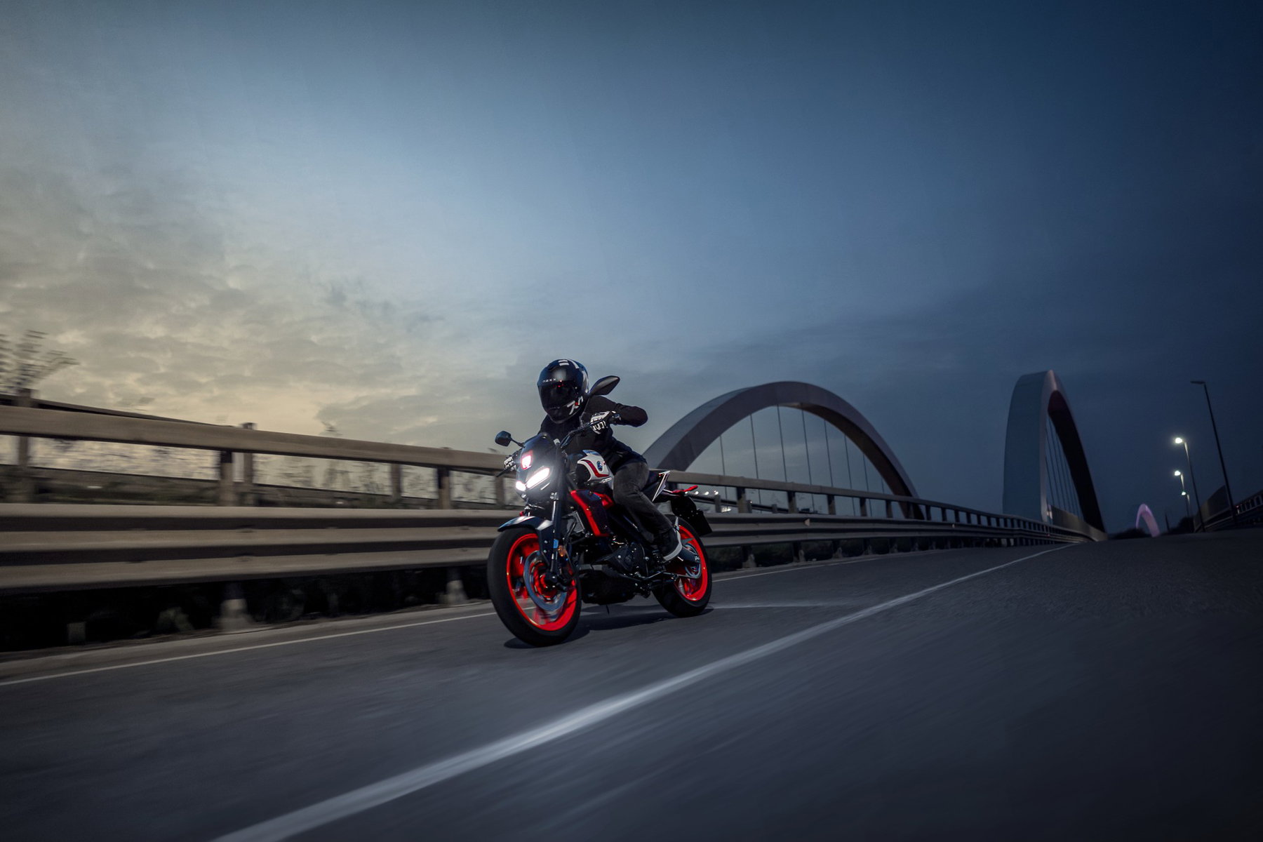 Yamaha MT-125 2027 – MT-125 in Redline White (Weiß mit roten Felgen und zweifarbiger Sitzbank) in Schräglage auf einer Brücke in der Abenddämmerung
