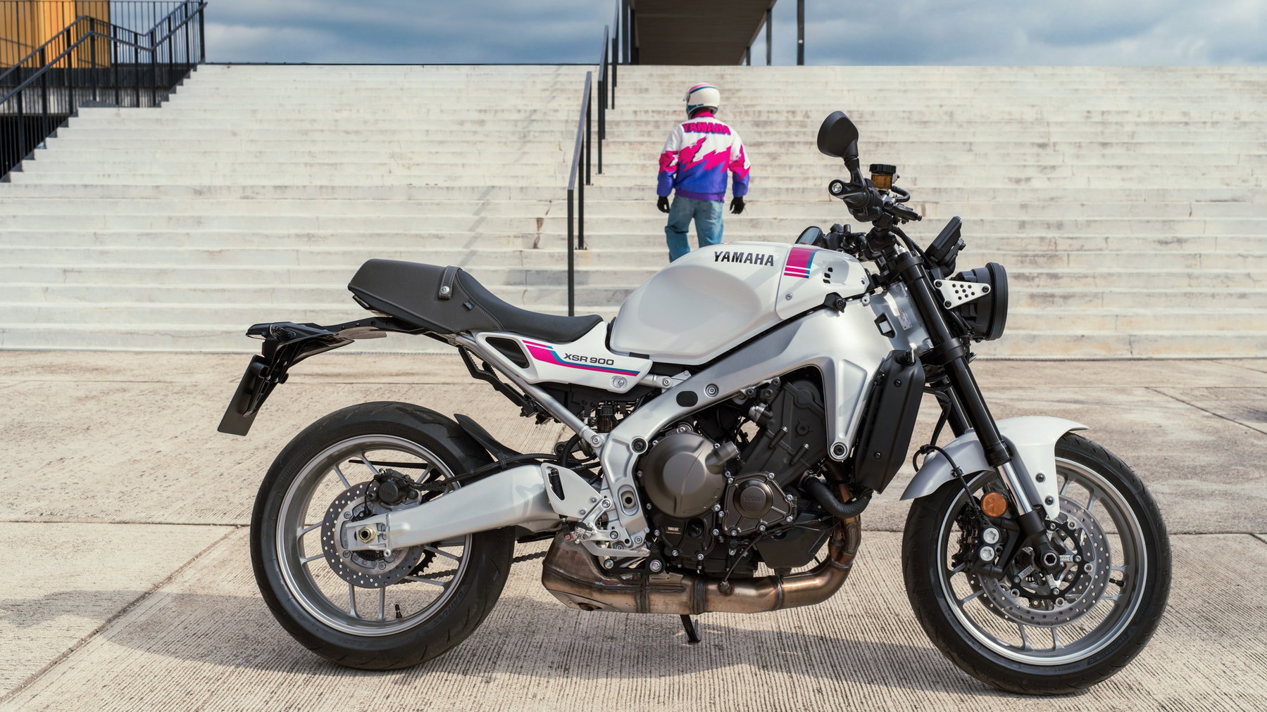 Yamaha XSR900 2027: Pink wie die YZF 750R, technisch bleibt alles gleich 1 Yamaha XSR900 2027 – Seitenansicht in Neon White mit pinken und blauen Akzenten vor einer Freitreppe