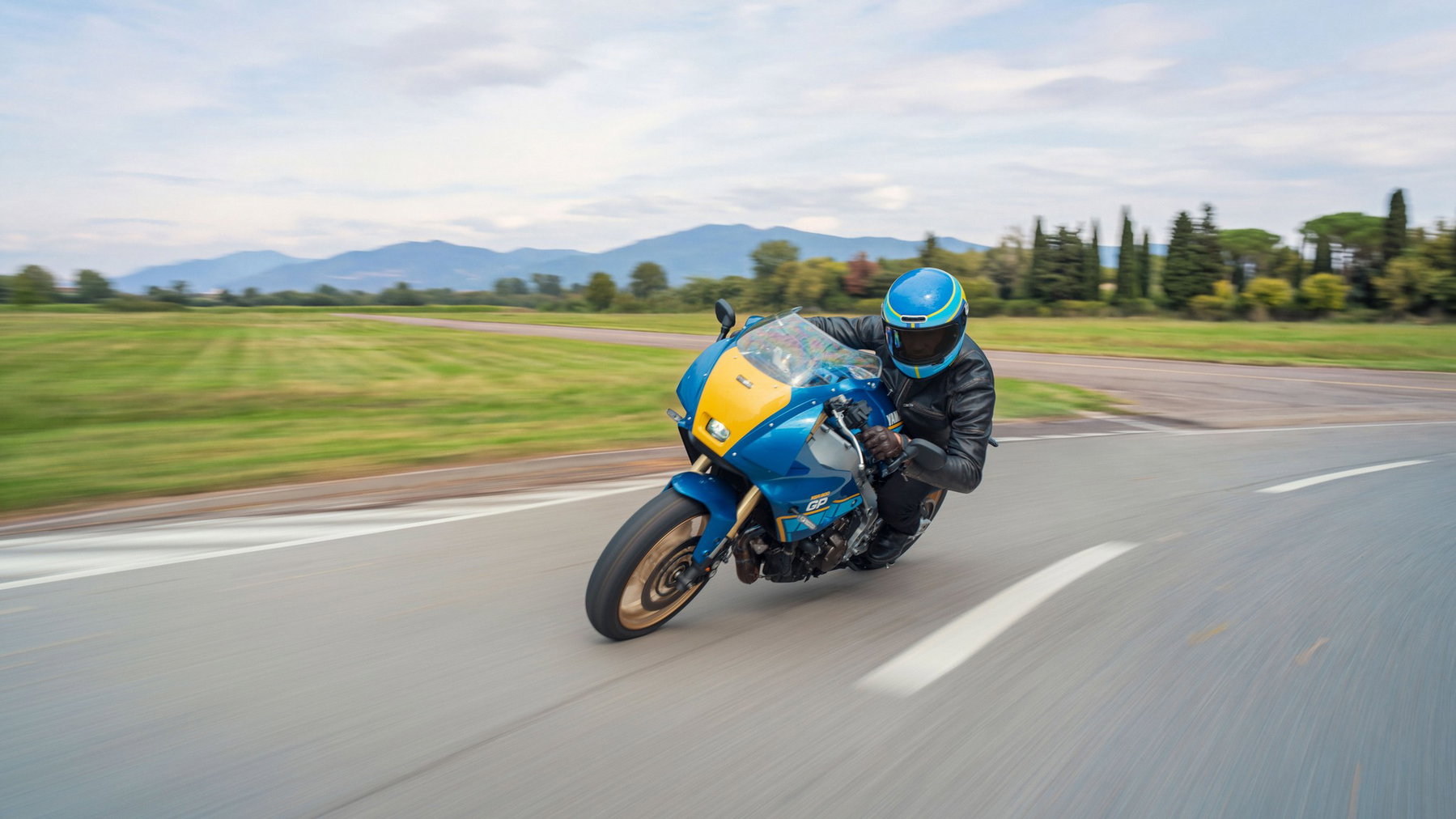 Yamaha XSR900 GP 2027 – in Legend Blue in Schräglage auf einer Piste vor Bergkulisse