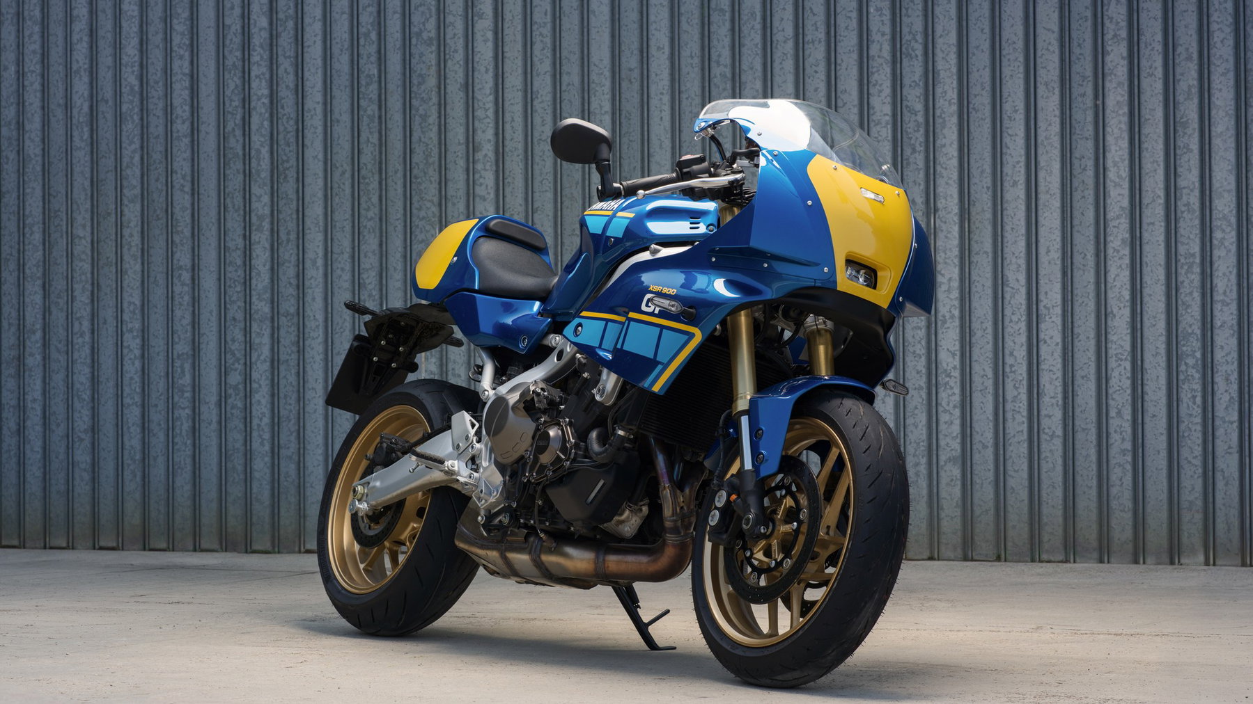 Yamaha XSR900 2027: Pink wie die YZF 750R, technisch bleibt alles gleich 5 Yamaha XSR900 GP 2027 – schräge Frontansicht in Legend Blue mit goldenen Felgen vor einer Wellblechwand