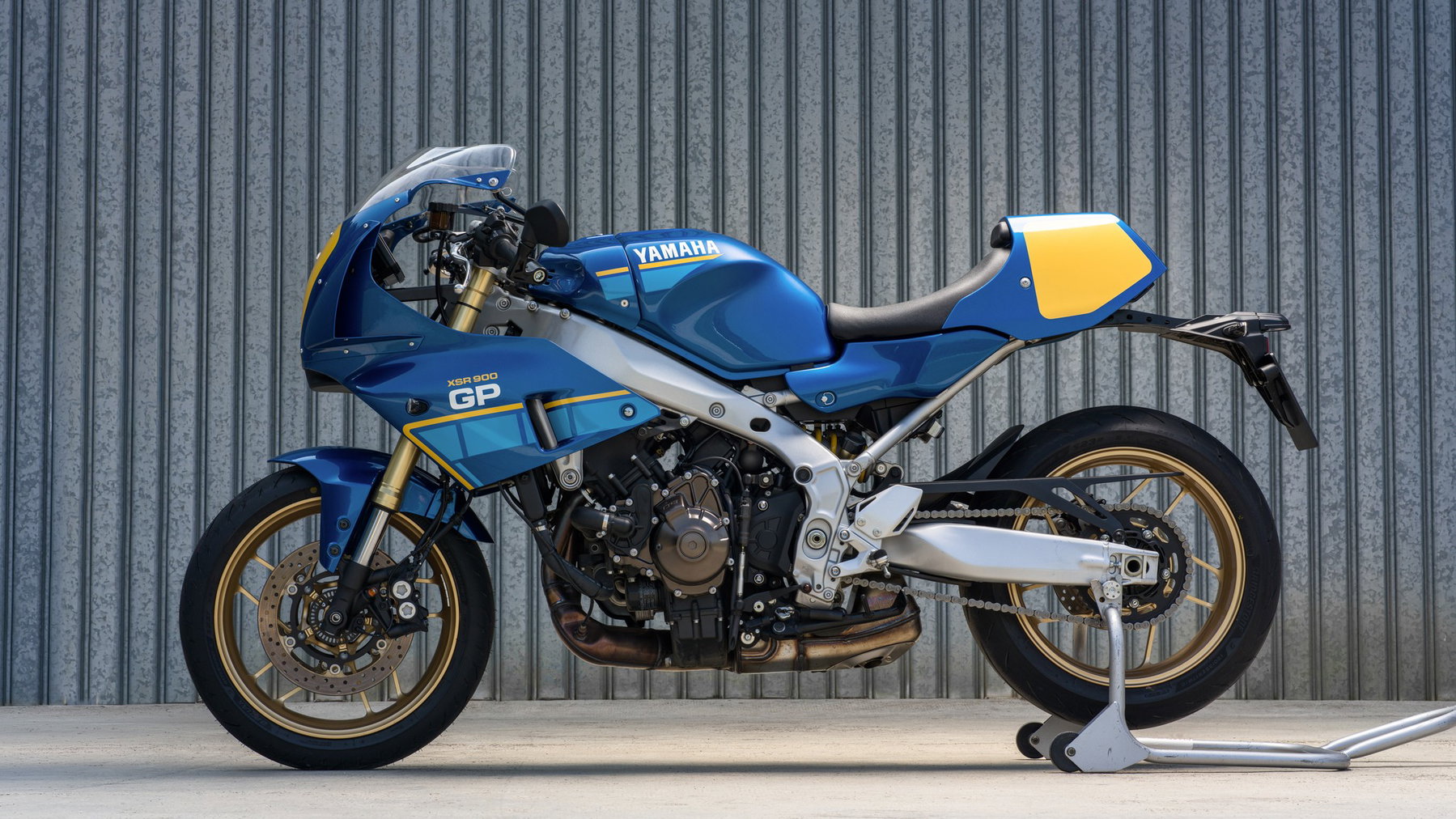 Yamaha XSR900 GP 2027 – Seitenansicht in Legend Blue auf Montageständer vor einer Wellblechwand