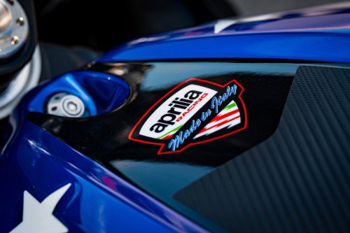 Aprilia Racing Made in Italy Emblem auf dem Tank der Aprilia X 250TH – Detailaufnahme mit blauer Stars-and-Stripes-Lackierung und Carbon-Einsatz