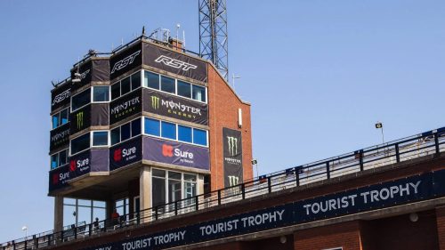 Kontrollturm und Grandstand der Isle of Man TT 2026 mit Sponsoren-Bannern von RST, Monster Energy und Sure – Tourist Trophy Rennstrecke
