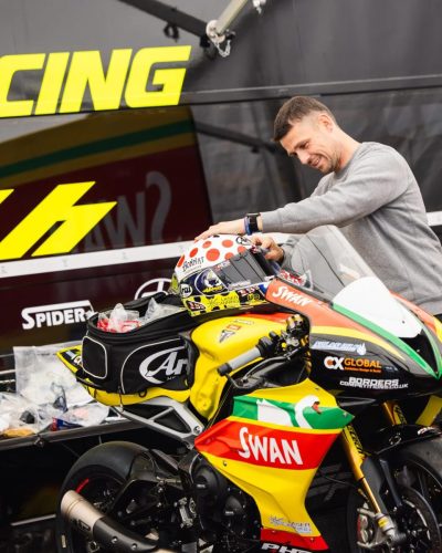 SWAN Racing Rennmaschine in Gelb-Rot-Gruen mit Arai Helm im Paddock – Isle of Man TT 2026