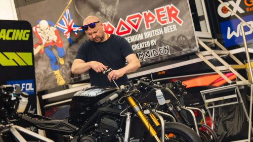 Mechaniker arbeitet an einer Rennmaschine vor dem Trooper Iron Maiden Banner – Isle of Man TT 2026 Paddock