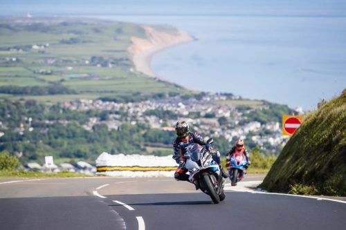 Zwei Newcomers-Solofahrer auf dem Mountain Course mit Kuestenpanorama – Isle of Man TT 2026 Speed Controlled Lap Bergabschnitt mit Einbahnstrassen-Schild