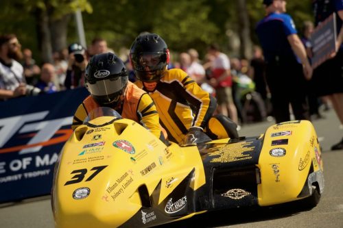 Sidecar Nr 37 Ellum Mannan Joinery SMH Racing Fahrer und Beifahrer am Start – gelbes Gespann mit Arai-Helm Isle of Man TT 2026 Newcomers TT-Banner