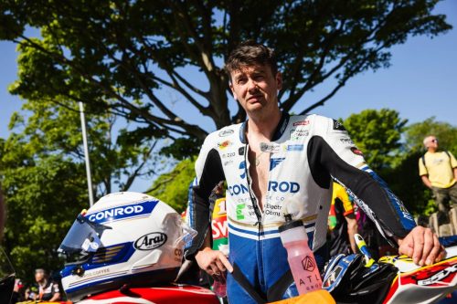 Fahrer in weiss-blauer Conrod Lederkombi mit Arai Helm im Sonnenschein – Isle of Man TT 2026