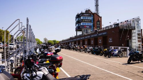 Geparkte Motorräder vor der TT-Grandstand-Tribüne bei Sonnenschein – Isle of Man TT 2026 Paddock