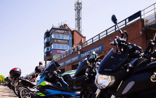 Fan-Motorräder vor dem Tourist-Trophy-Turm mit Monster-Energy-Banner – Isle of Man TT 2026 Paddock