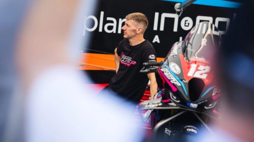 Ian Hutchinson mit Startnummer 12 im Team-RST-Shirt neben seinem Motorrad im Paddock – Isle of Man TT 2026