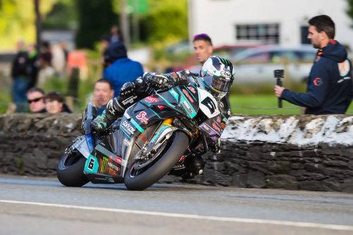 Michael Dunlop auf der Hawk Racing Honda Nummer 6 in Schräglage vor Zuschauern an Steinmauer – Isle of Man TT 2026 Qualifying