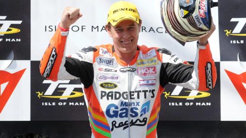 John McGuinness jubelt mit erhobener Faust und Helm in der Hand in Padgett's Manx Gas Racing Lederkombi auf dem Podium - Senior TT, Isle of Man TT 2008
