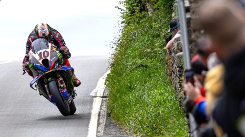 Peter Hickman auf der BMW mit Startnummer 10 im Wheelie bergauf auf oeffentlicher Strasse, Zuschauer filmen hinter der Steinmauer - Senior TT Preview, Isle of Man TT 2026