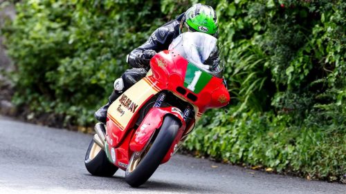 Mike Browne auf der rot-cremefarbenen Melbray-Paton mit Retro-Tribut-Lackierung in Schraeglage zwischen gruenen Hecken auf dem Mountain Course - Sportbike TT Race 1, Isle of Man TT 2026