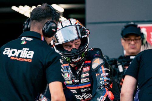 Marco Bezzecchi mit geöffnetem Helmvisier im Gespräch mit einem Aprilia-Racing-Techniker in der Box – MotoGP Großbritannien GP Silverstone 2026