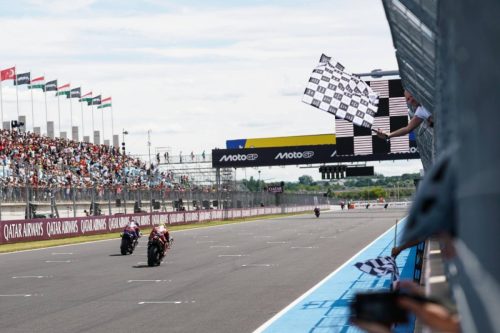 Schwenkende Zielflagge über der Strecke mit Joan Mir im Feld – MotoGP Ungarn GP Balaton Park 2026