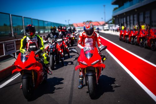 Ducati-Werksfahrer in roten Lederkombis auf ihren Motorrädern in der Boxengasse der World Ducati Week 2026