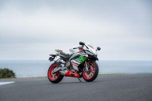Aprilia RS 660 Phillip Island Tribute in Weiß mit grünen Seitenteilen und roten Felgen, schräg von vorn rechts auf der Rennstrecke von Phillip Island, im Hintergrund das Meer