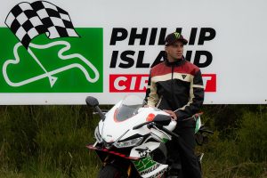 Marco Bezzecchi lehnt an der Aprilia RS 660 Phillip Island Tribute vor dem Schild des Phillip Island Circuit