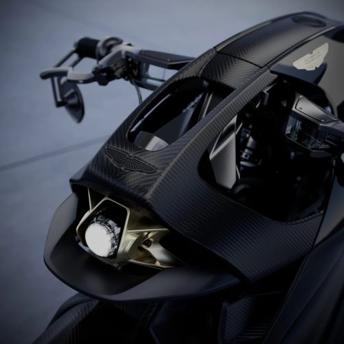 Aston Martin AMB 002 (2027) – Detailansicht des Scheinwerfers mit goldfarbener Fassung und Aston-Martin-Flügelemblem auf der Carbon-Verkleidung